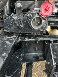 Volvo truck component close-up with red 2-pin power inlet and wiring near a circular black cap, metal brackets, and textured frame.