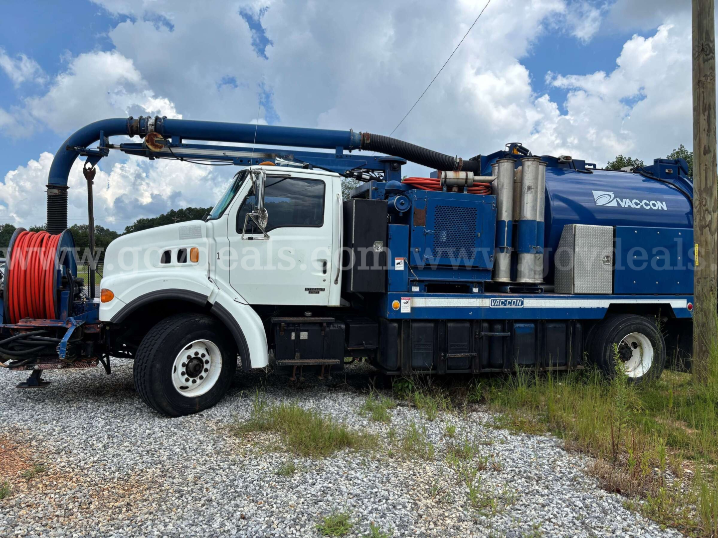 Sterling L7500 vacuum truck with white cab and blue vacuum unit, side view showing hose reel and storage compartments.
