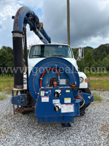 Truck-mounted vacuum system on a white cab with blue debris tank, front view showing hose reel and intake, Sterling L7500 truck.
