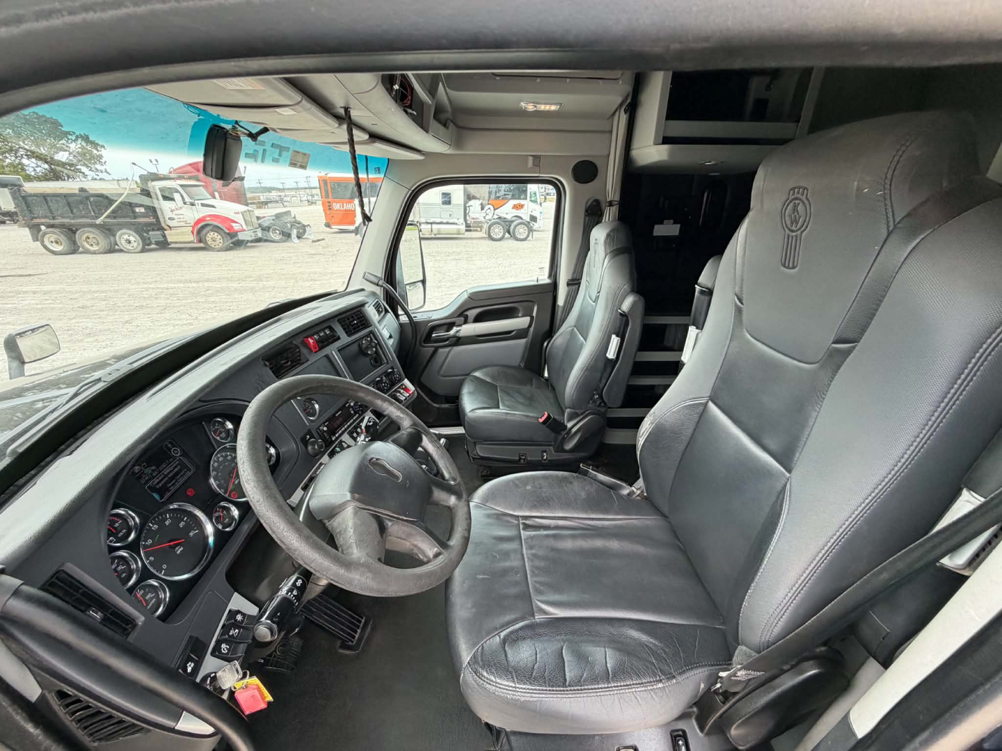 Kenworth T680 cab interior showing steering wheel, dashboard gauges, driver seat, and passenger seat.