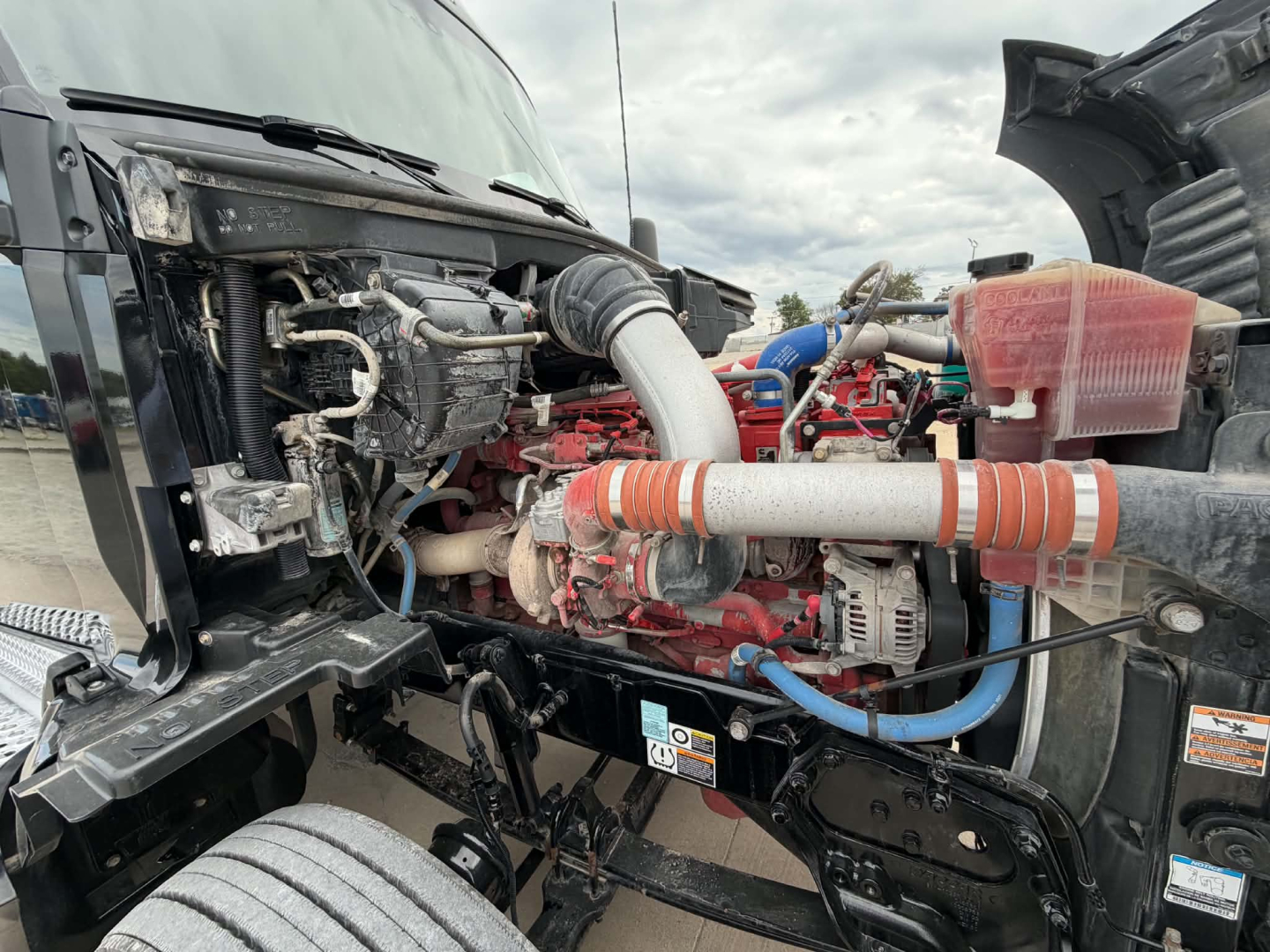 Kenworth T680 engine bay showing engine block, hoses, alternator, and cooling system components.