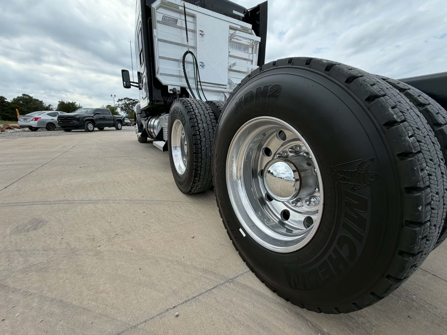 Kenworth T680 truck front wheel and side of cab showing polished chrome wheels and dual rear tires with fuel and exhaust compartments visible