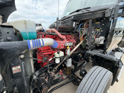 Kenworth T680 engine bay showing a red Cummins ISX engine with blue silicone coupler, wiring harness, coolant reservoir, and exposed components.