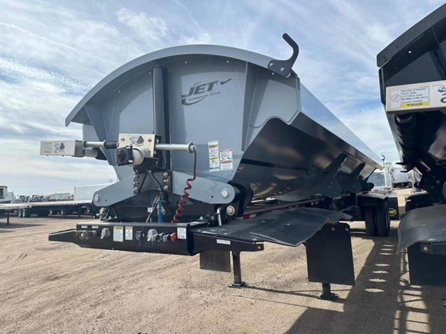 Jet brand jet air ride side dump trailer in service view showing front hitch, hydraulic lines, and lifting arm with Jet logo.