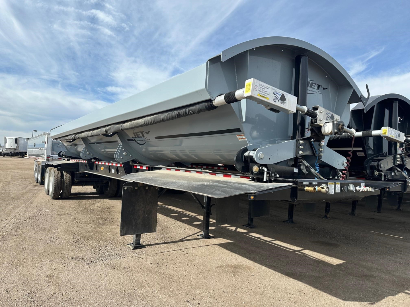 Jet Air Ride Side Dump trailer showing long gray cargo bed with undercarriage and dual axle wheels, hydraulic components near front, and support stands.