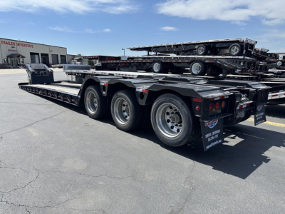 Load King RGn lowboy trailer with triple-axle rear, flatbed sections, and ramp/auger visible; other trailers stacked in background.