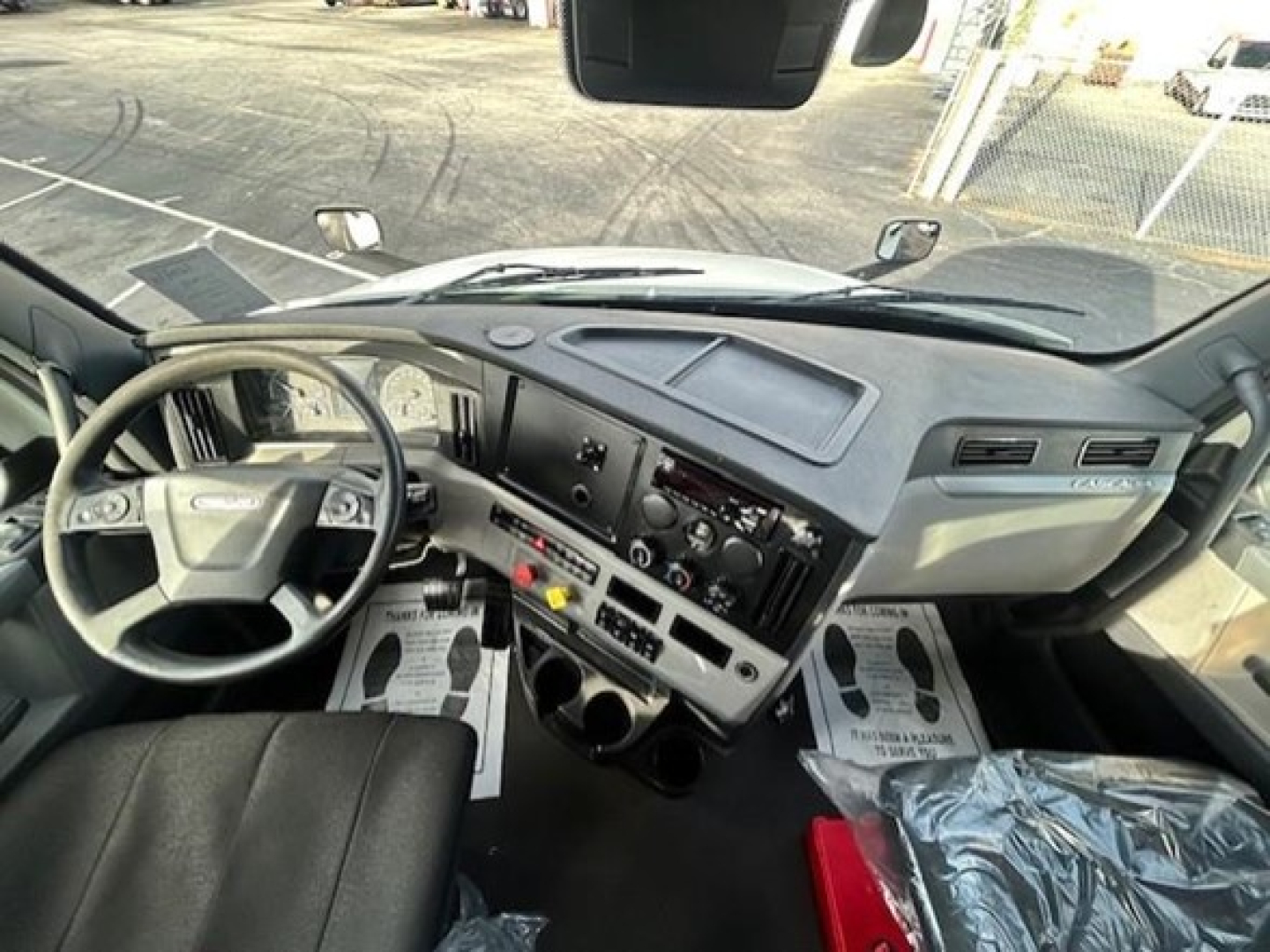 Cab interior of a 2021 Freightliner Cascadia 126 day cab showing steering wheel, dashboard with gauges, control panel, center stack, and driver floor mats.