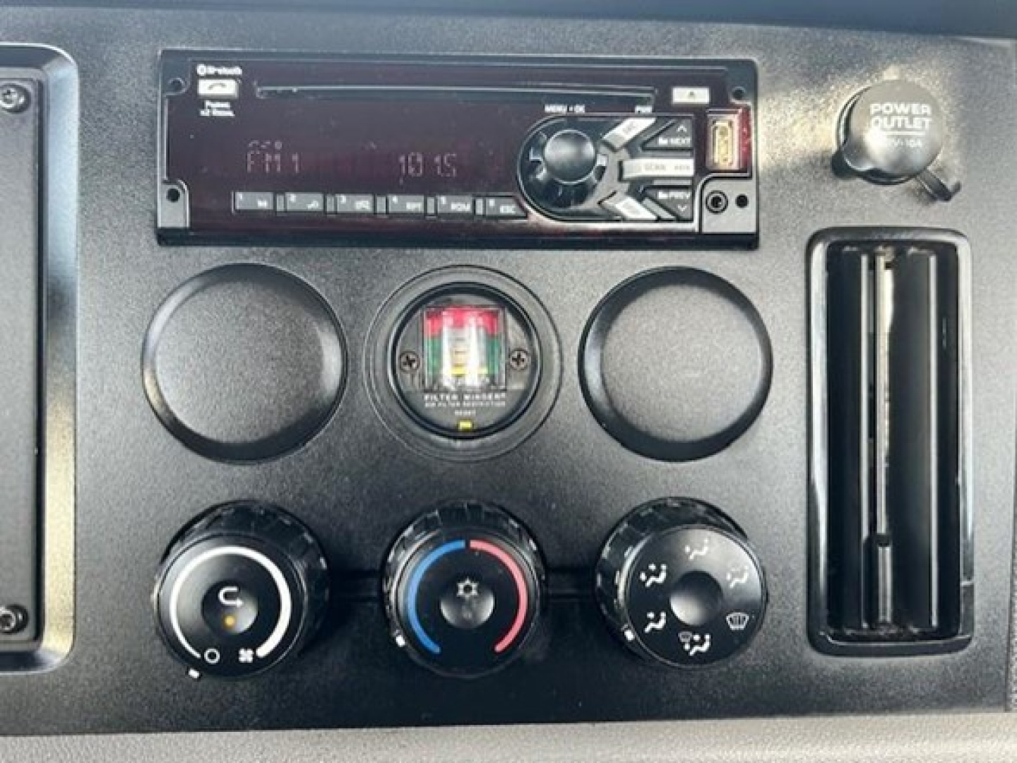 Dashboard of a Freightliner Cascadia 126 showing radio head unit, air conditioning dials, and a power outlet.