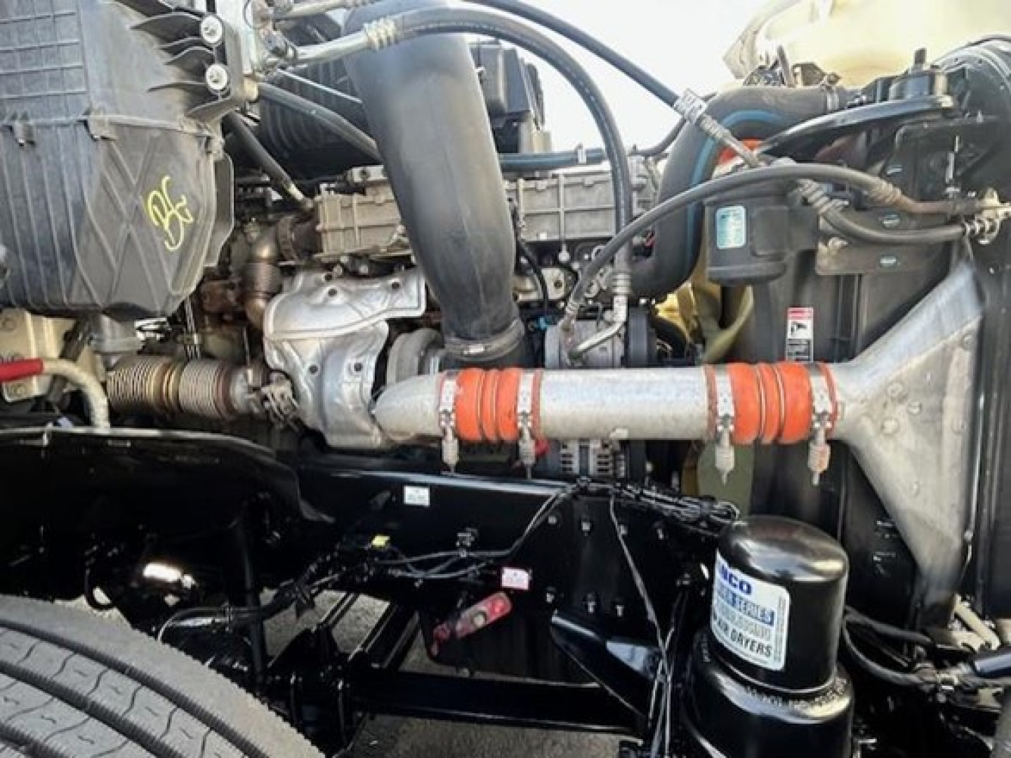 Freightliner Cascadia 126 engine bay showing coolant reservoir, air filter canister, hoses, and engine components with orange hose clamps.