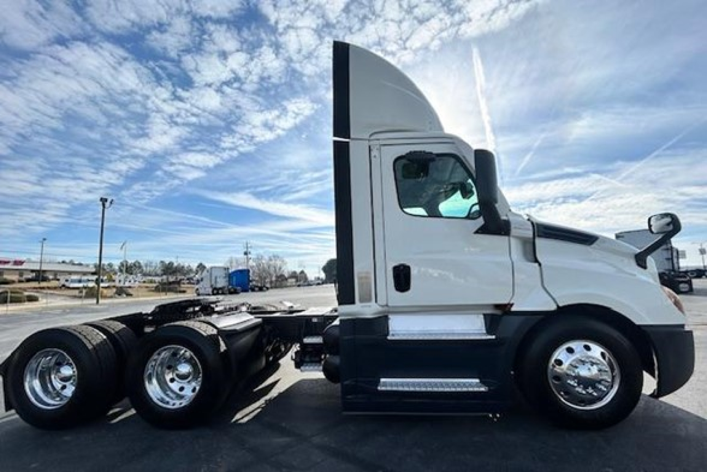 Truck side view showing 2021 Freightliner Cascadia 126 day cab with sleeperless hood, twin rear axles, chrome wheels, and white cab.