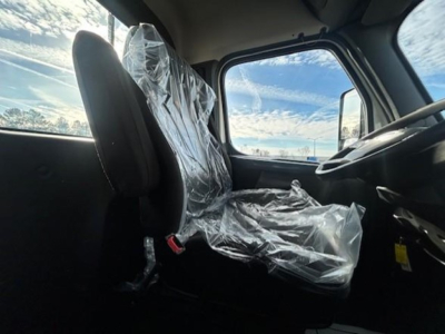 Cab interior of a Freightliner Cascadia 126 with plastic seat cover on the driver seat, steering wheel, and dashboard visible.