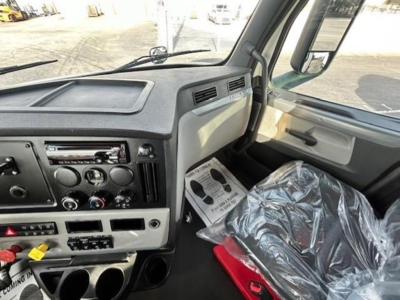 Cab interior of a 2021 Freightliner Cascadia 126 day cab showing steering wheel, dashboard controls, and plastic-wrapped seat.