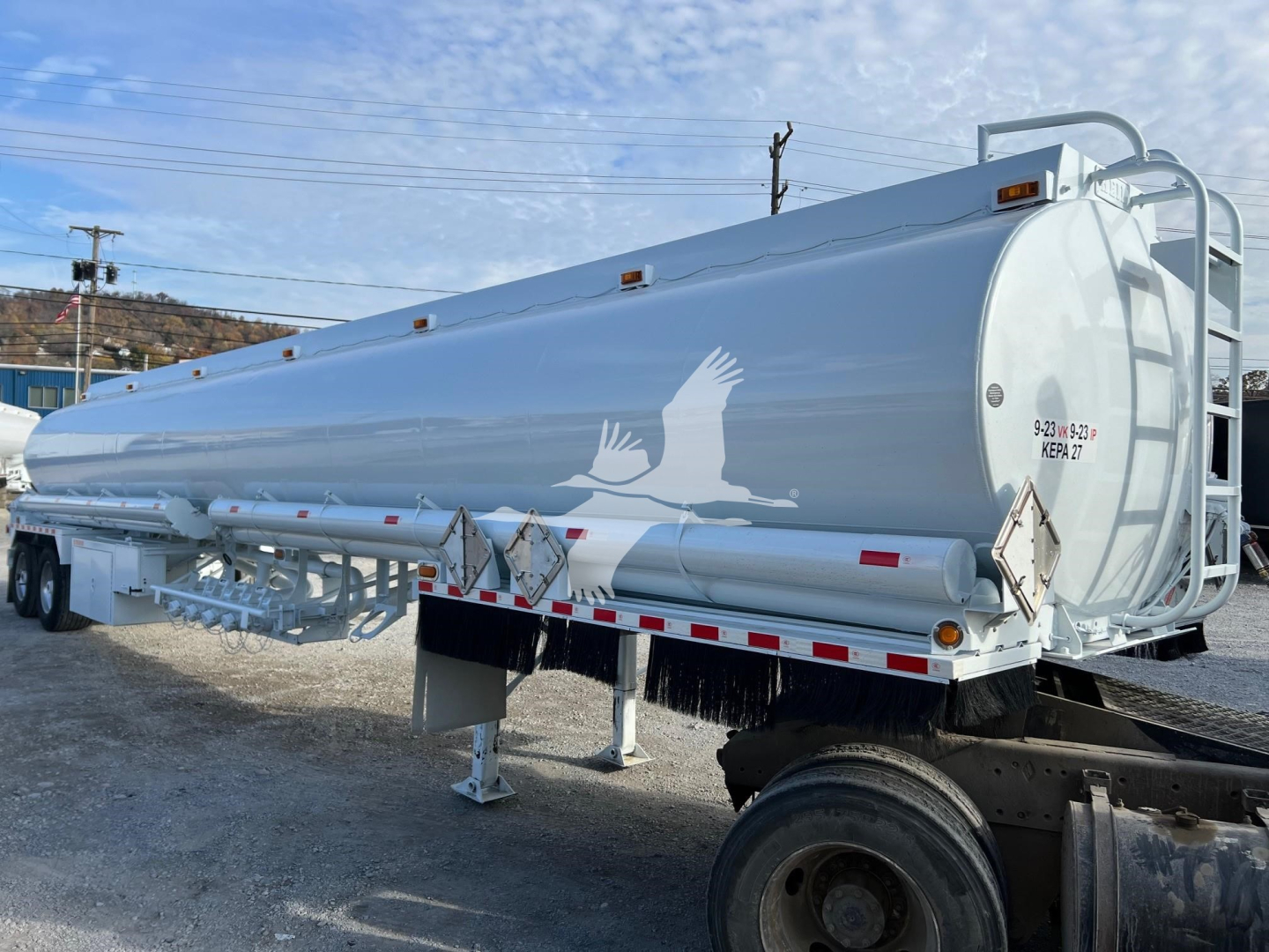 Bottom Petro tank trailer showing cylindrical white Heil trough tank with ladder and support legs.