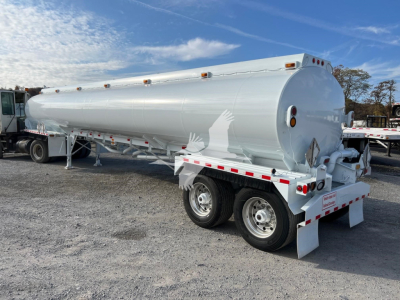 Tank trailer showing a white Heil trough bottom petro tank mounted on a dual-axle trailer with rear visibility lights and safety markings.