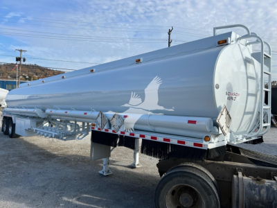 Bottom Petro tank trailer showing cylindrical white Heil trough tank with ladder and support legs.