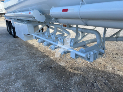 Fuel tanker trailer underside with multiple valves and piping for Heil trough bottom petro tank, light gray components, toolbox, and hoses attached.