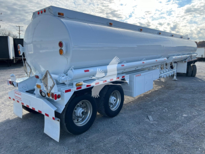 Petro tank trailer showing cylindrical white Heil trough bottom fuel tank with dual rear axle, rear lights, and support ladder; side access compartments; VIN tag not visible.