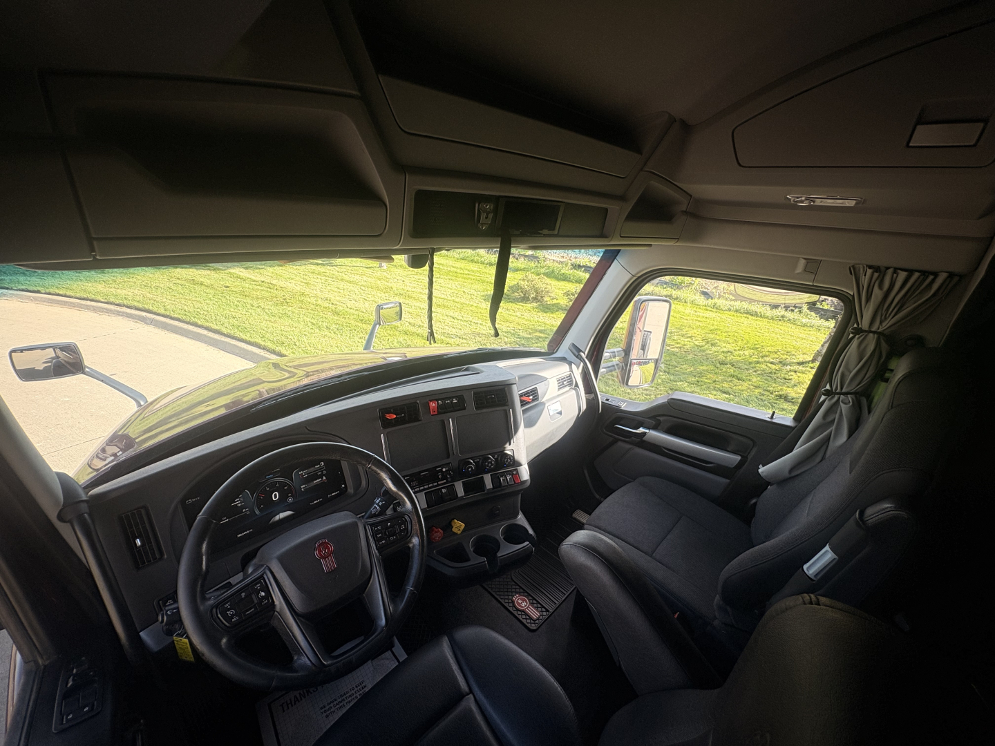 Kenworth truck interior showing dashboard and steering wheel with a grey interior; visible are instrument cluster, center console, and driver seat.