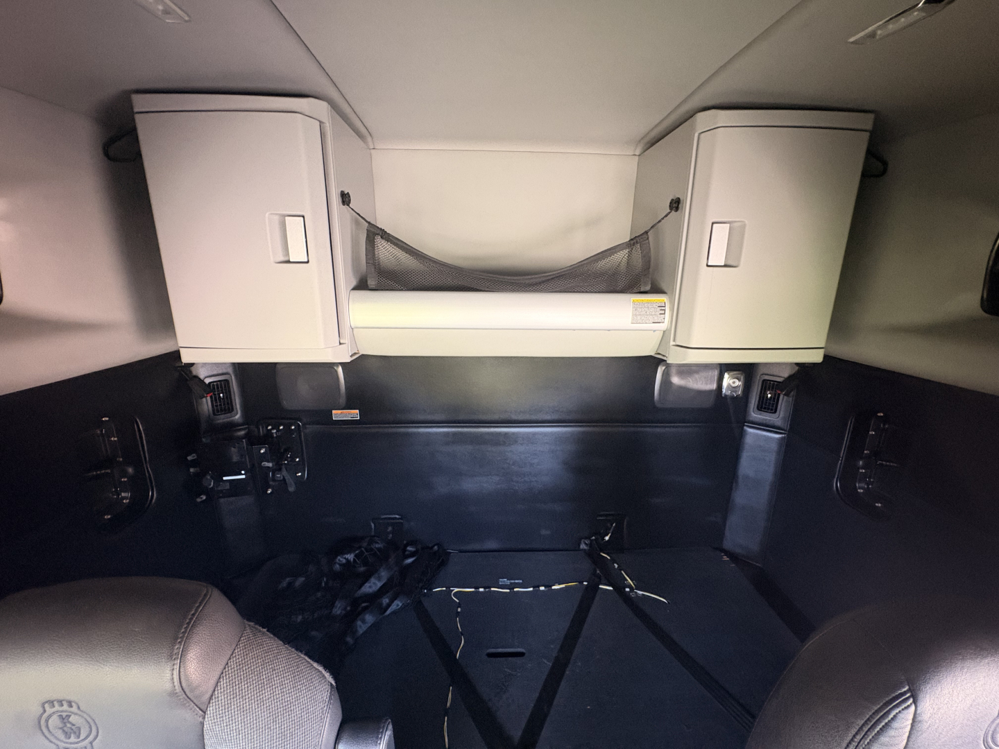 Kenworth T680 sleeper cab interior showing overhead cabinets and storage net with bed area.