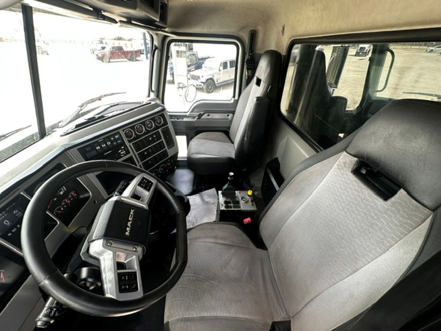 Cab interior of a 2020 Mack GR64F dump truck showing steering wheel with Mack logo, dashboard controls, and front seats.