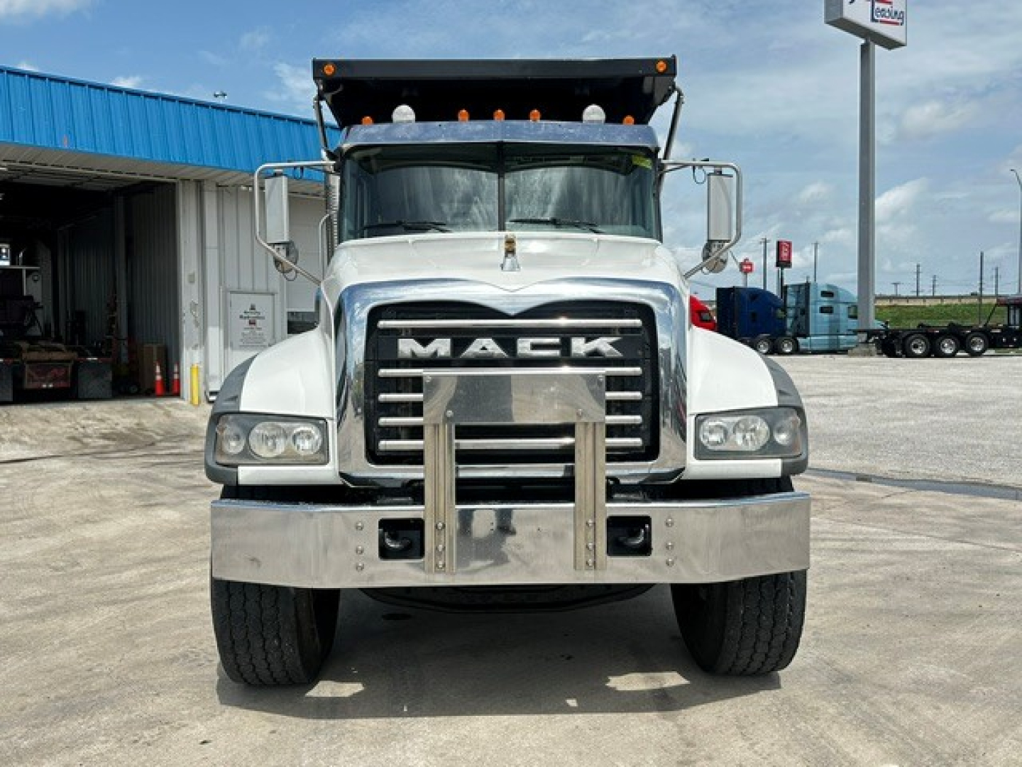Front view of a Mack dump truck showing large grille with MACK lettering, bumper guard, headlights, and a chrome front bumper.