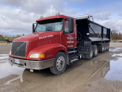 Volvo dump truck with red cab and black dump body, front left view. Visible text on door and hood: '231-627-9298' and 'EXCAVATING LANDSCAPIN' (partially), license plate area. No other legible labels clearly visible.