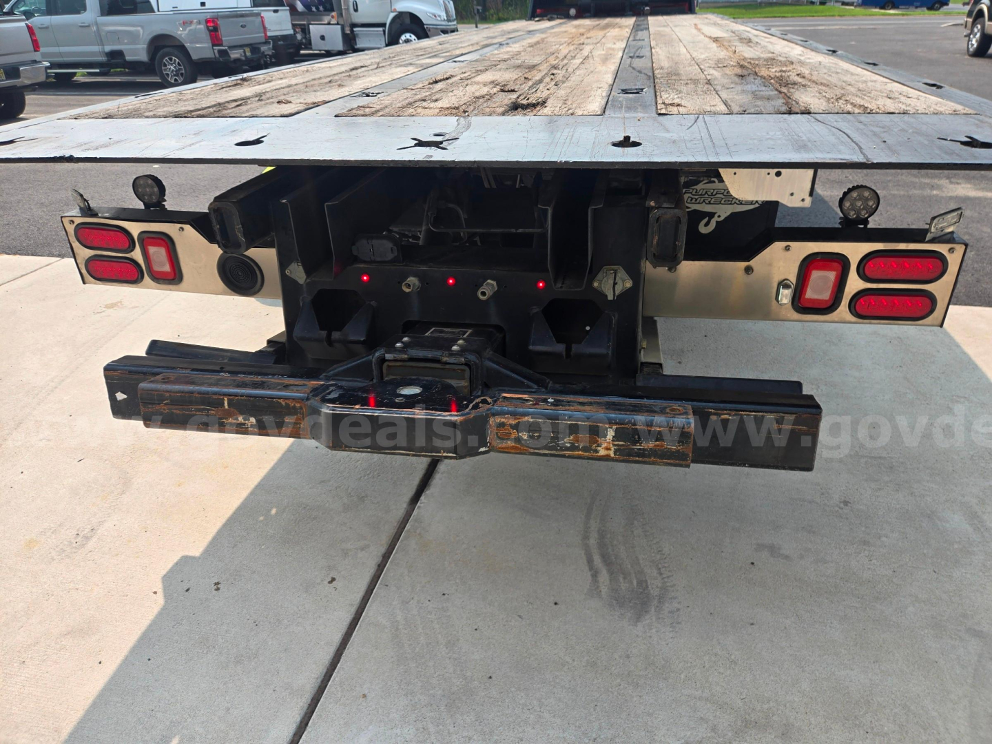 Rear view of a Freightliner M2 flatbed truck chassis showing tail lights, bumper, hitch plate, and wooden deck.
