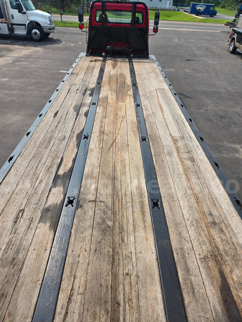 Flatbed tow truck bed with wooden planks and metal rails, rear cab in background, Freightliner M2 listing details visible in context.