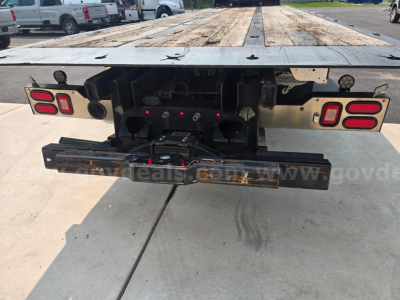 Rear view of a Freightliner M2 flatbed truck chassis showing tail lights, bumper, hitch plate, and wooden deck.