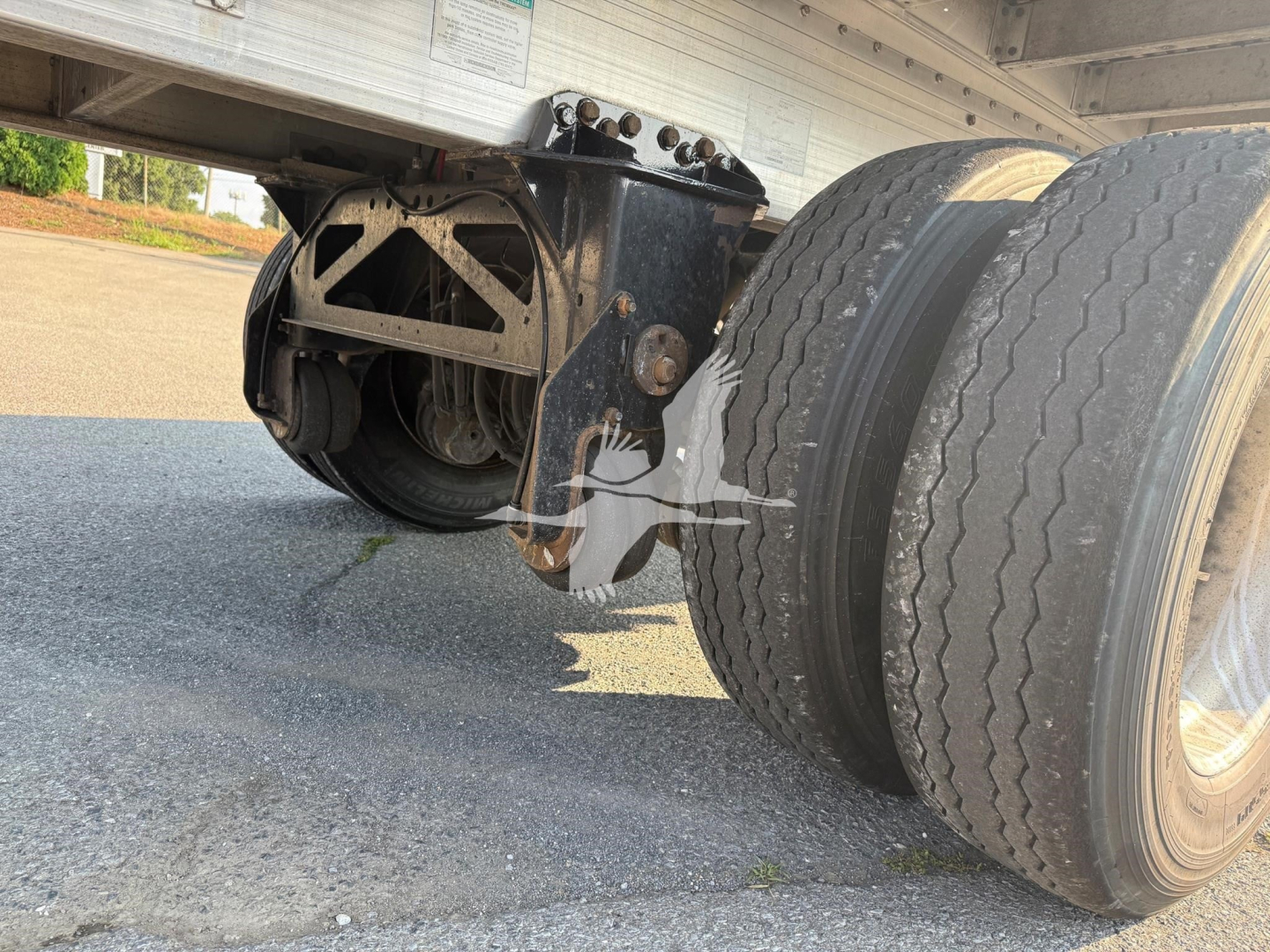 Trailer undercarriage showing dual rear axles and suspension components with wheel tires and metal frame.