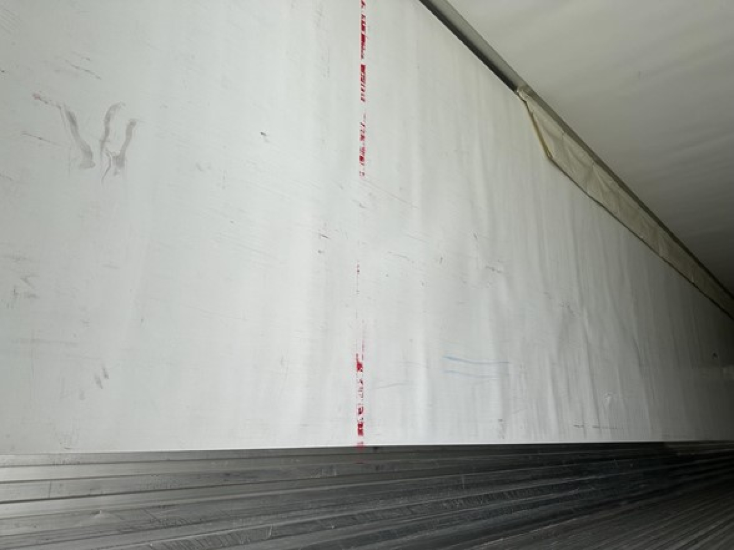  Trailer interior wall in a reefer trailer showing blank white surface with faint red tape marks.