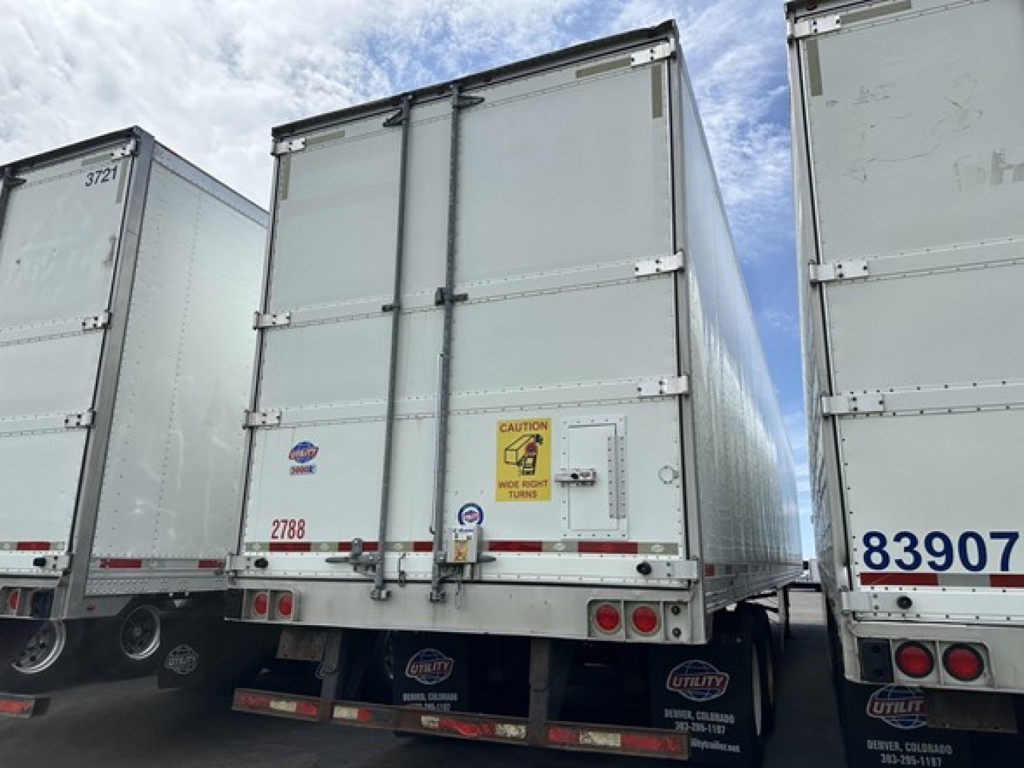 Rear view of a used 2018 Utility 3000R reefer trailer showing rear doors, taillights, and bumper with a safety sticker, part of a row of similar trailers.