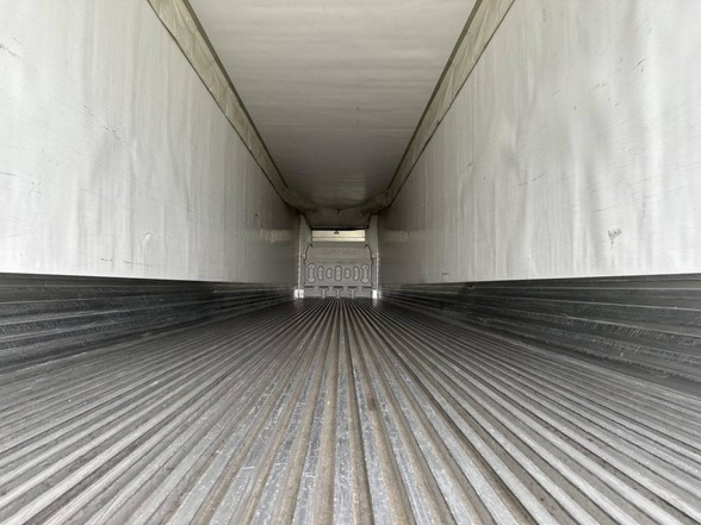 Inside trailer cargo area with ribbed floor and white walls; rear door tail area visible with tape and numbers; no other legible text.