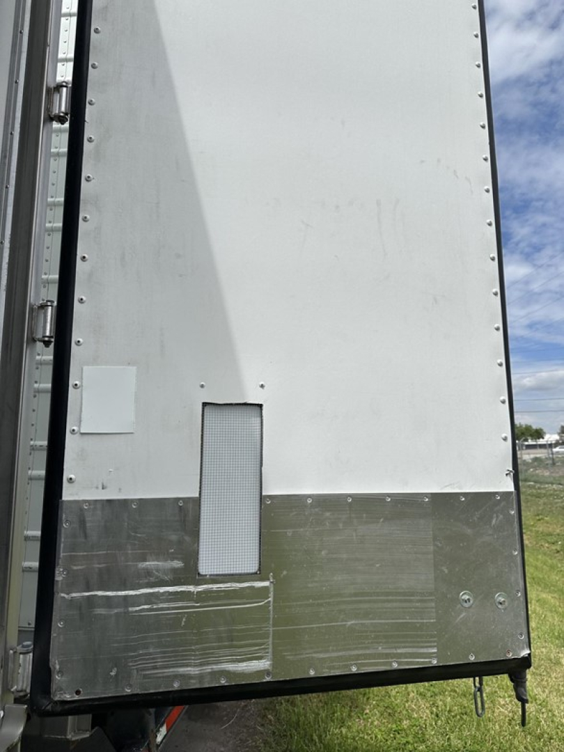 Vertical rear of a Utility 3000R reef trailer showing a rectangular access panel and lower metal kick plate; riveted seam along the edge and a small vent window.