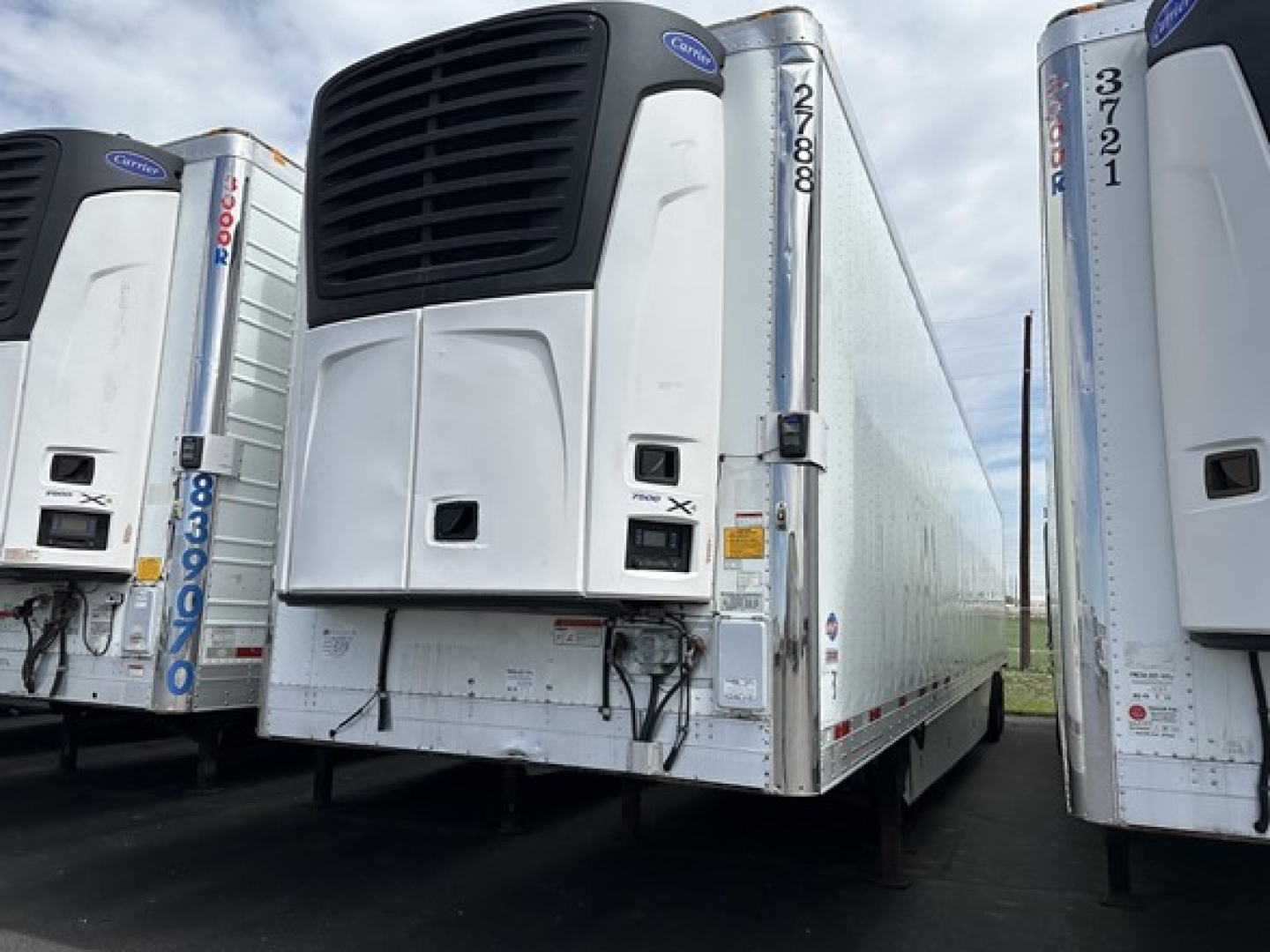 Utility 3000R trailer refrigeration unit with black front cooling grille and white body, side doors, and multiple trailers in a row.