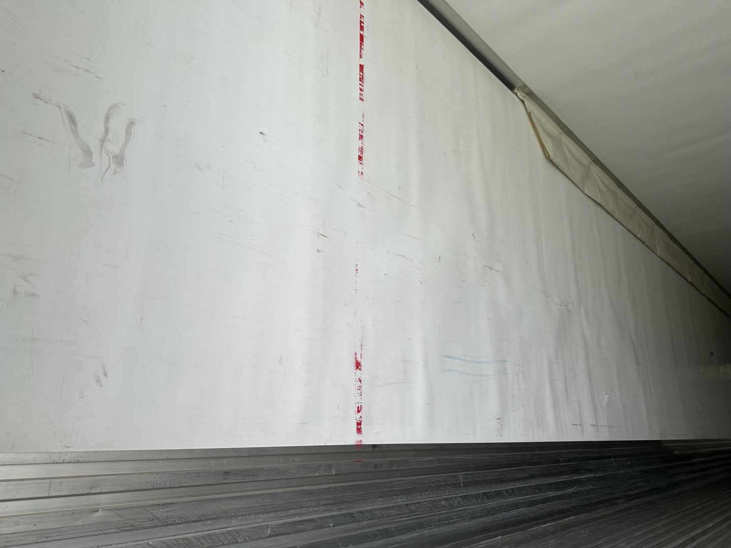Trailer interior side wall withWhite aluminum surface and ribbed floor edge.