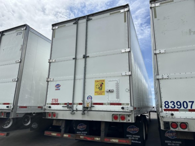 Rear view of a used 2018 Utility 3000R reefer trailer showing rear doors, taillights, and bumper with a safety sticker, part of a row of similar trailers.