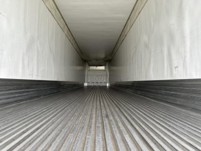 Inside trailer cargo area with ribbed floor and white walls; rear door tail area visible with tape and numbers; no other legible text.