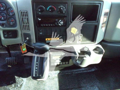 Truck cab interior focusing on gear shifter, steering column, dashboard with gauges, and a built-in control panel; visible labels and warning sticker on center console.
