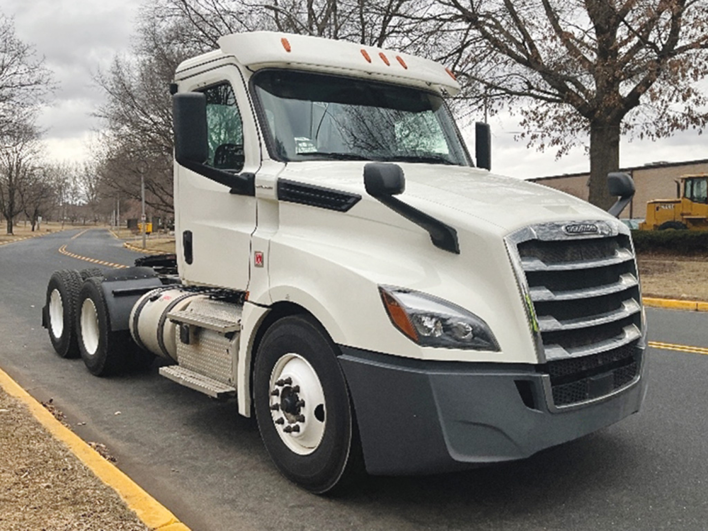White Freightliner Cascadia126 semi-truck cab, front left side, with dual rear axles and black bumper. No visible text on truck body.