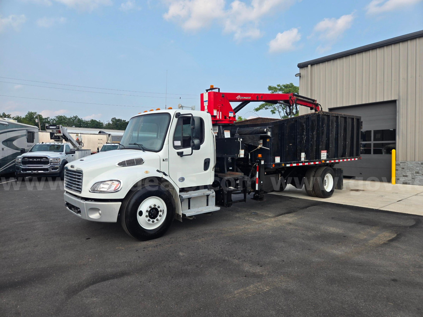 2019 Freightliner M2 grapple truck with a red crane arm on a black flatbed. White cab, side mirrors, large front grille, stock number 29174-85 visible.