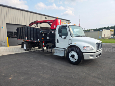 Truck side view of a 2019 Freightliner M2 grapple truck with a red crane and black hopper/storage bed, white cab, in a dealership lot.