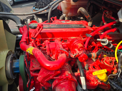 Red diesel engine bay with various hoses, belts, and yellow dipstick handle visible in a Freightliner M2 grapple truck.