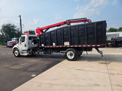Truck equipped with a black dump body and red hydraulic crane/overhead grapple on a Freightliner M2 chassis, side view showing stock number 29174-85 and multiple warning decals.