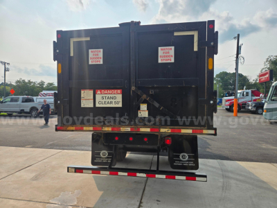 Freightliner M2 dump truck rear showing safety decals and bumper; two rear doors with signs: 'DANGER STAND CLEAR 50''; additional labels 'WATCH FOR SUDDEN STOPS' on each door; rear underride guard and tail lights visible.