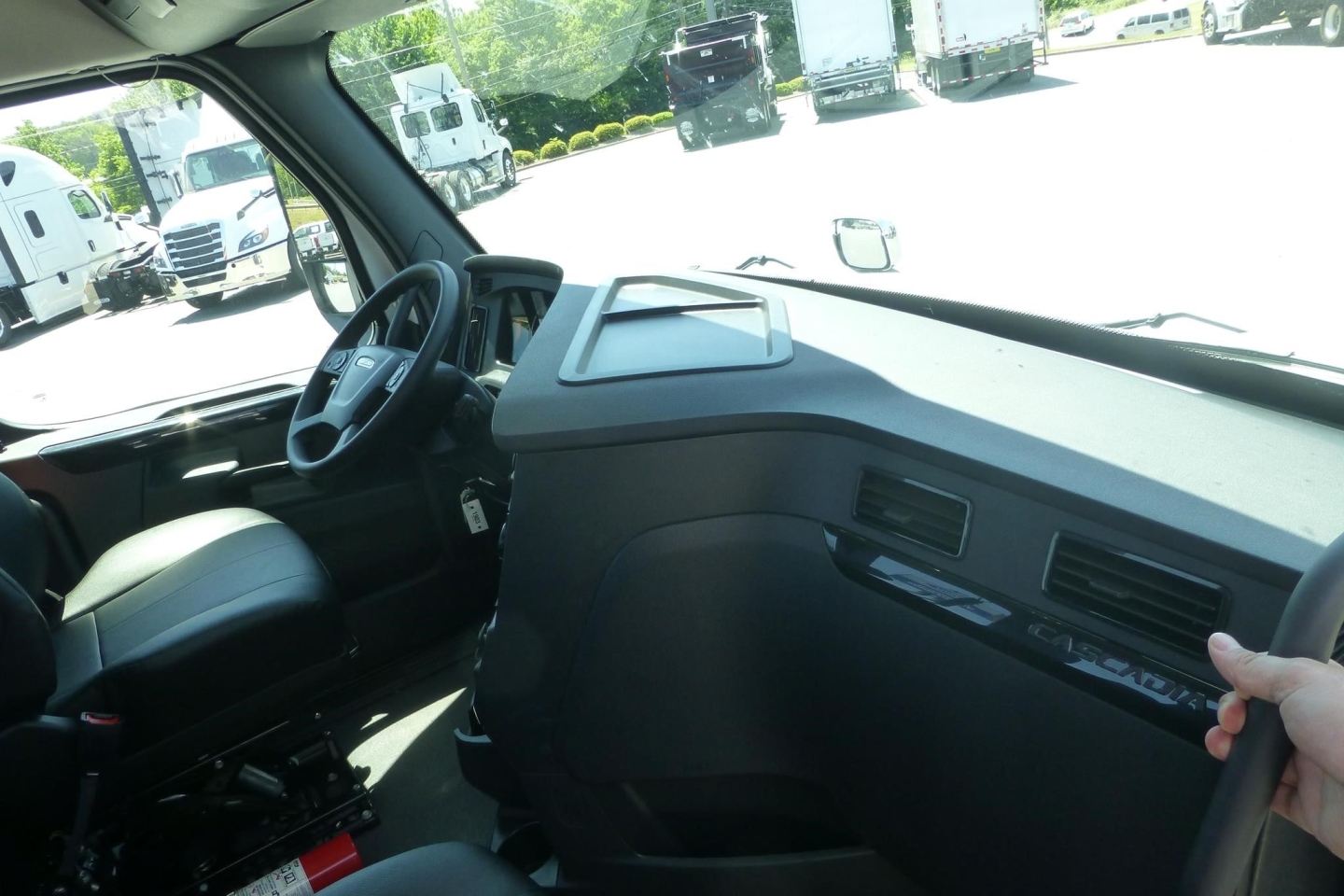 Freightliner Cascadia truck cockpit interior with steering wheel, dashboard, and passenger seat visible in daytime showroom lot.