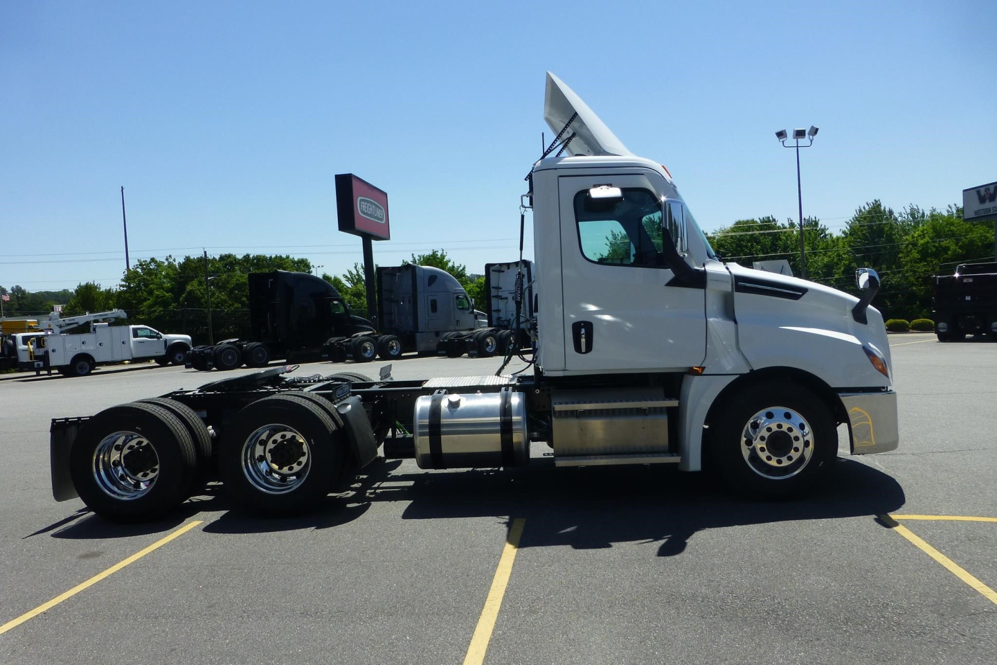 Freightliner Cascadia day cab truck side view showing chassis and wheels in a dealership lot with other trucks in background.