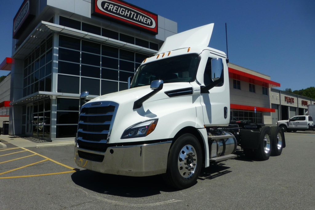 Truck front-left view of a white 2027 Freightliner Cascadia day cab parked outside dealership showing chrome bumper and grille.