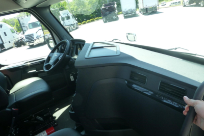 Freightliner Cascadia truck cockpit interior with steering wheel, dashboard, and passenger seat visible in daytime showroom lot.