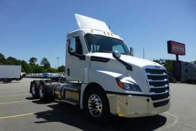 White Freightliner Cascadia day cab truck in a dealership lot, front/driver side view with chrome bumper and exhaust, hood logo visible.